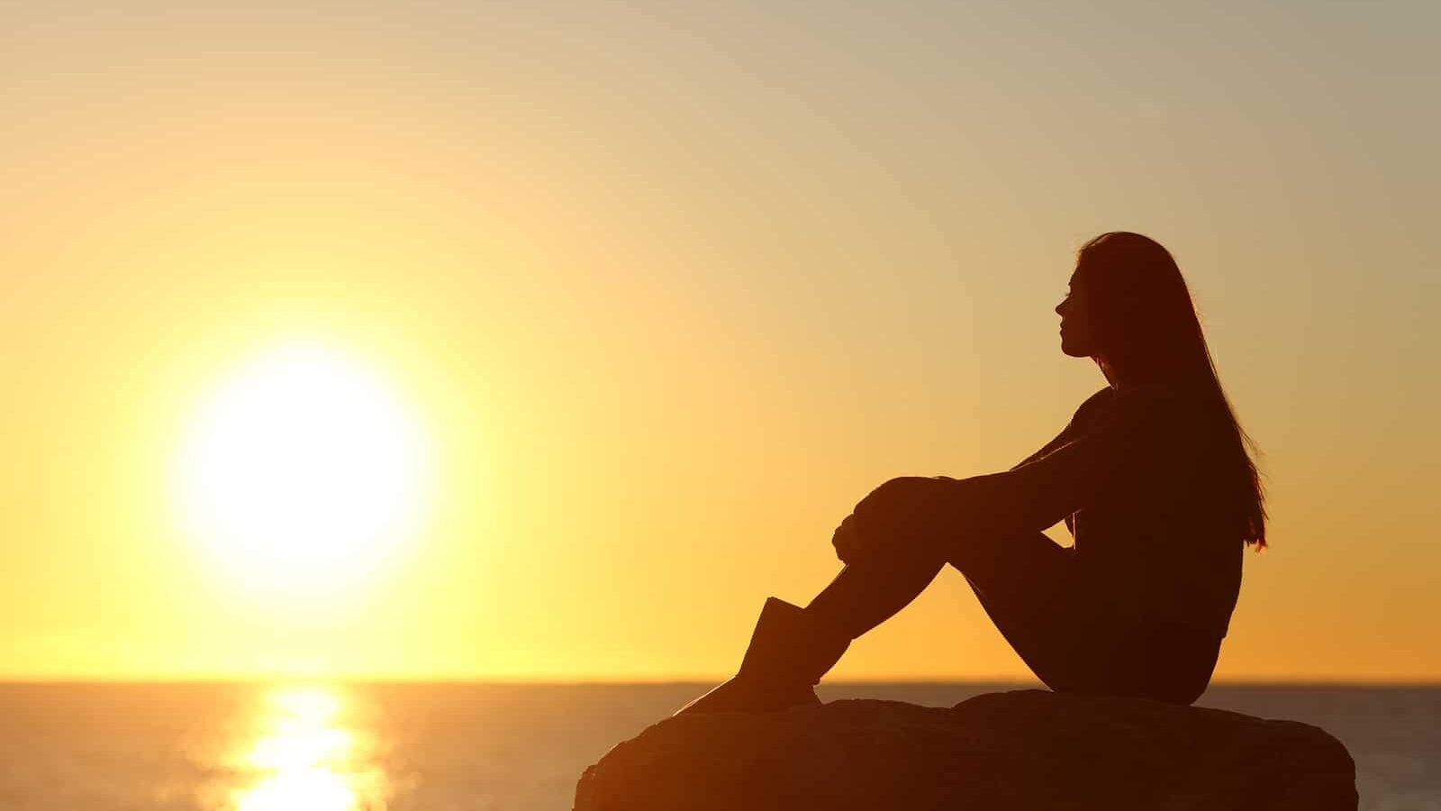 Profile of a woman silhouette watching sun on the beach at sunset