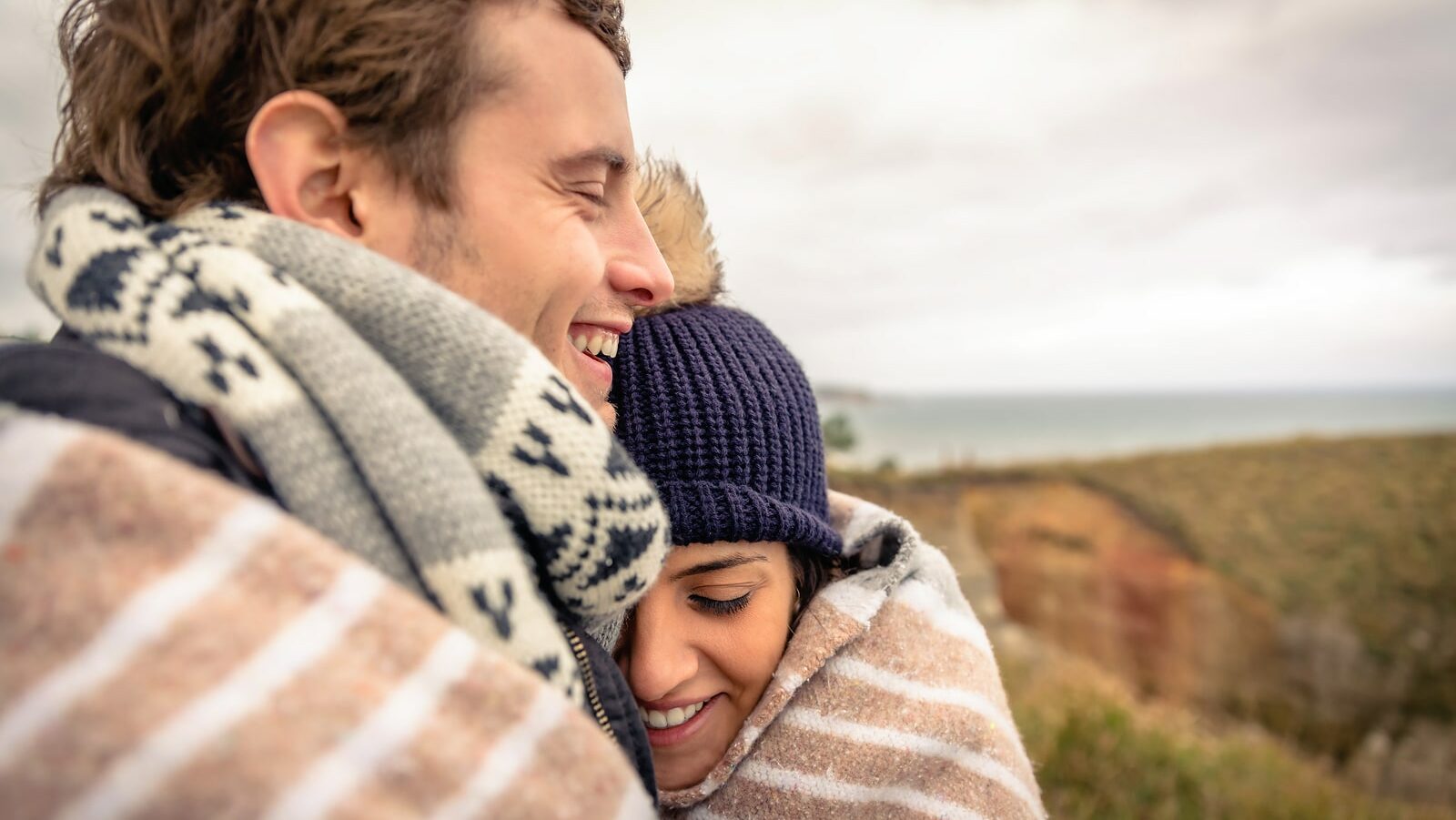 Young couple laughing outdoors under blanket in a cold day