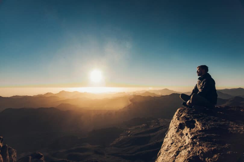 Homem sentado na beira de um penhasco, observando o horizonte.