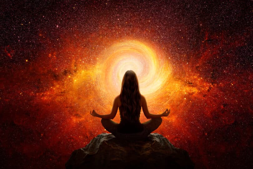 Silhueta de mulher meditando em frente a um buraco de luz laranja e vermelha