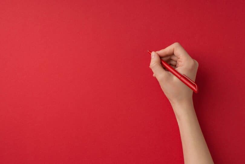 Mão segurando uma caneta vermelha sobre um papel vermelho