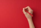 Mão segurando uma caneta vermelha sobre um papel vermelho
