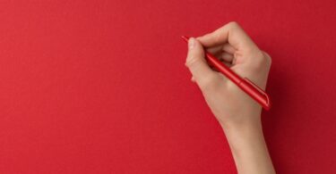 Mão segurando uma caneta vermelha sobre um papel vermelho