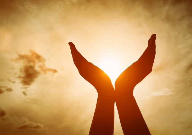 Mãos levantadas em oração ao céu com lindo sol ao fundo