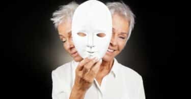 imagem de uma senhora segurando uma máscara na frente de seu rosto, um lado tem a representação de sua feição triste e a outra com feição de felicidade