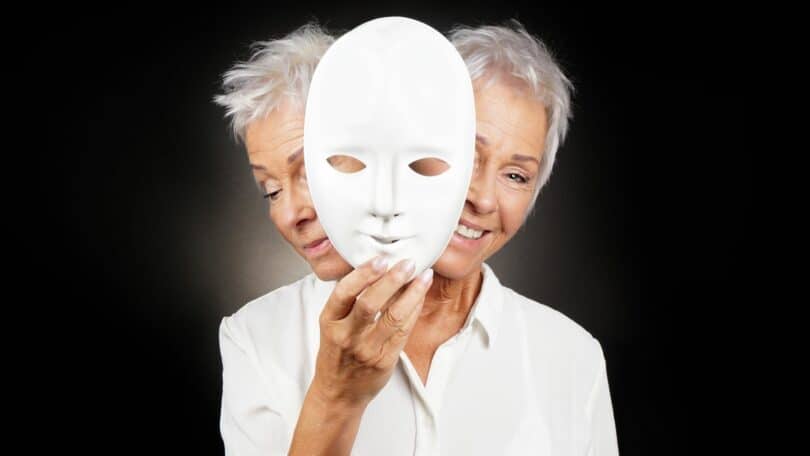 imagem de uma senhora segurando uma máscara na frente de seu rosto, um lado tem a representação de sua feição triste e a outra com feição de felicidade