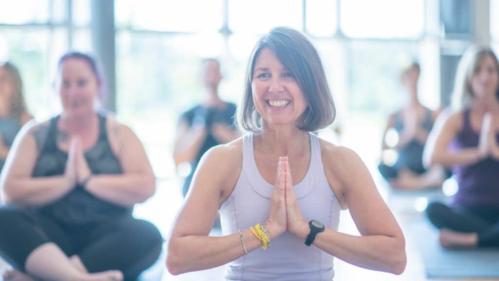 Imagem de uma mulher em postura de Yoga sorrindo e outras mulheres ao fundo da imagem
