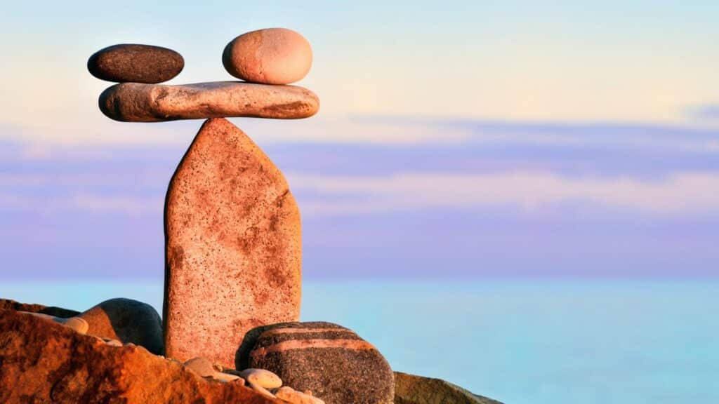 Imagem de pedras em equilíbrio e ao fundo uma paisagem de céu azulado e arroxeado