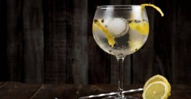 Imagem de uma taça de Gin em uma mesa, com uma colher e limão do lado em um fundo escuro