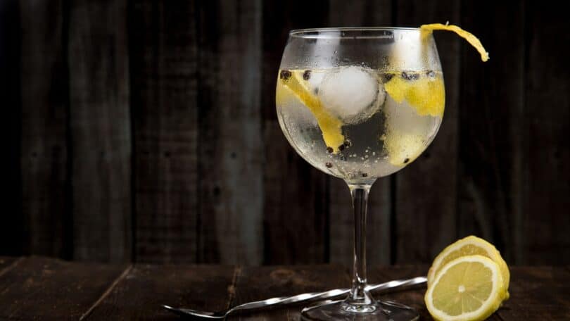 Imagem de uma taça de Gin em uma mesa, com uma colher e limão do lado em um fundo escuro