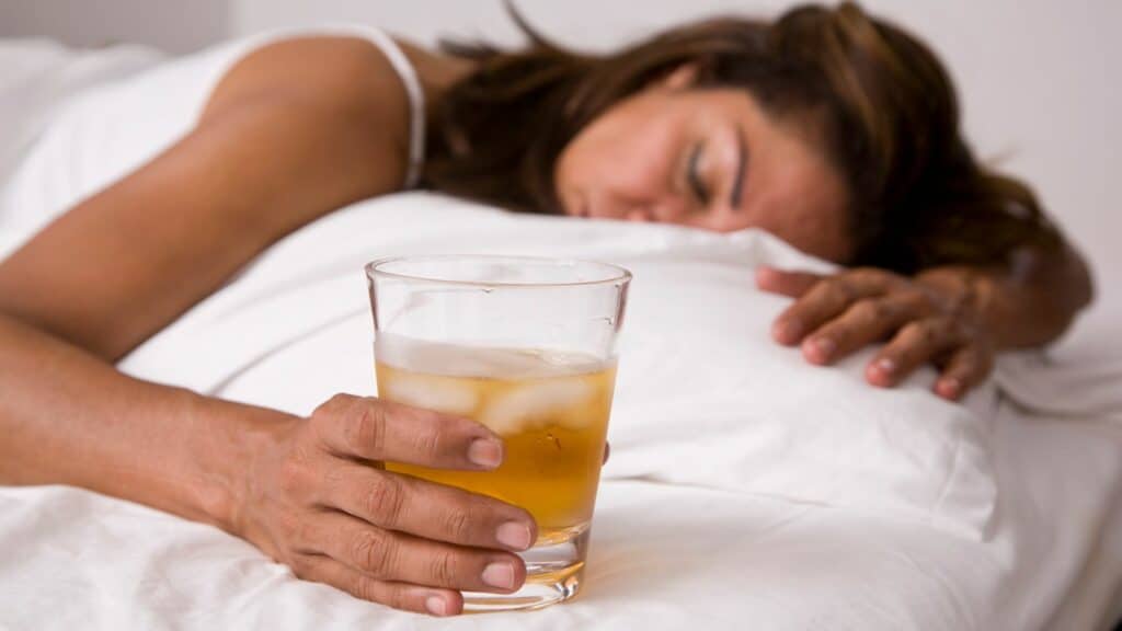 Imagem de uma mulher dormindo com um copo de bebida alcoólica na mão