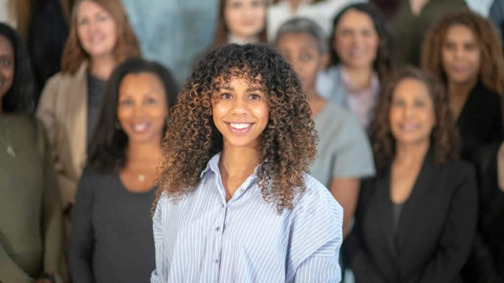 Imagem de várias mulheres, uma está mais no foco da imagem e as outras atrás, mas todas sorrindo