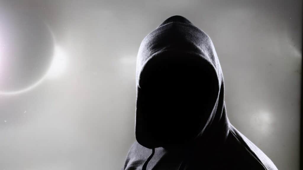 Imagem de uma pessoa, que parece um fantasma, de capuz e sem rosto e um fundo cinza