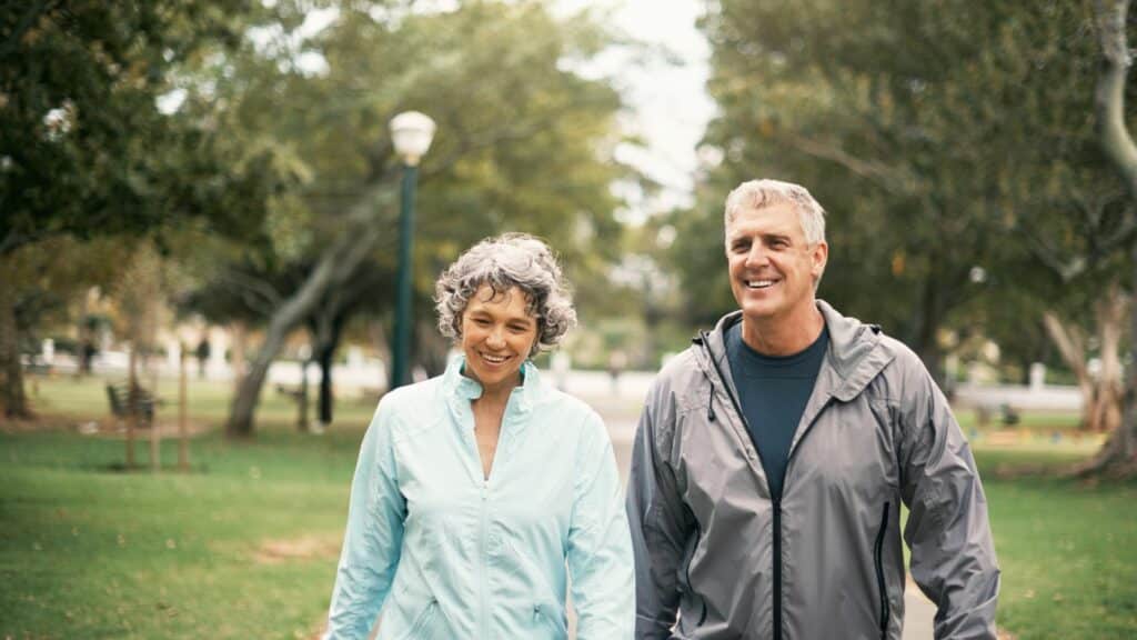 Imagem de um casal de meia idade sorrindo e caminhando no parque.