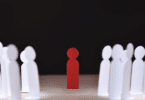 Pessoas feitas de papel branco encarando uma pessoa de papel vermelha