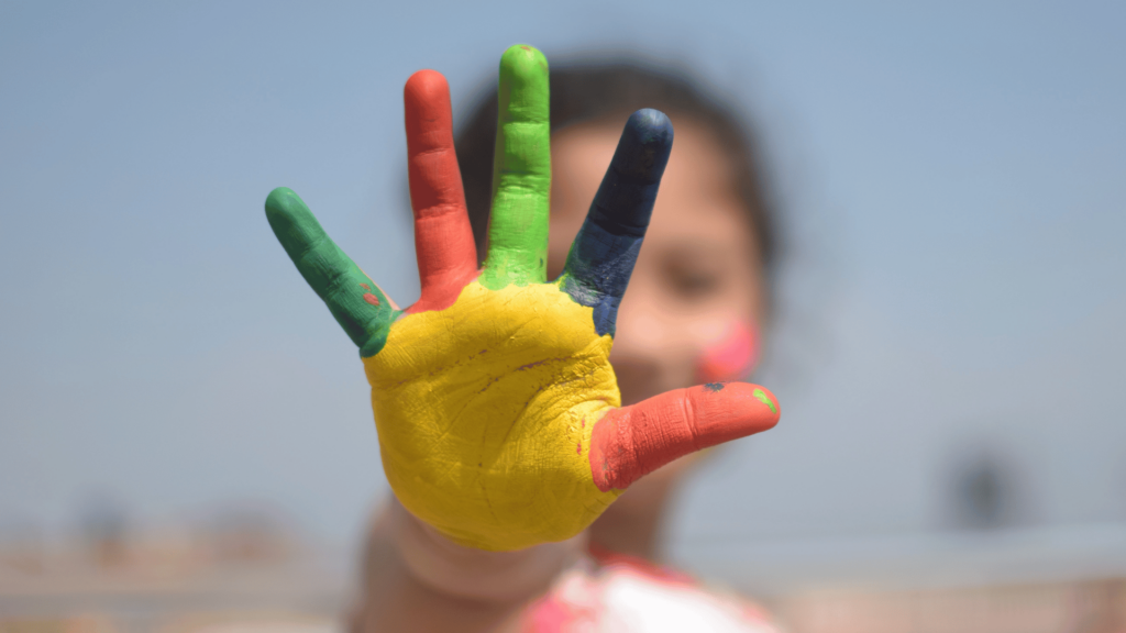 Criança com os dedos pintados, mostrando a palma da mão.