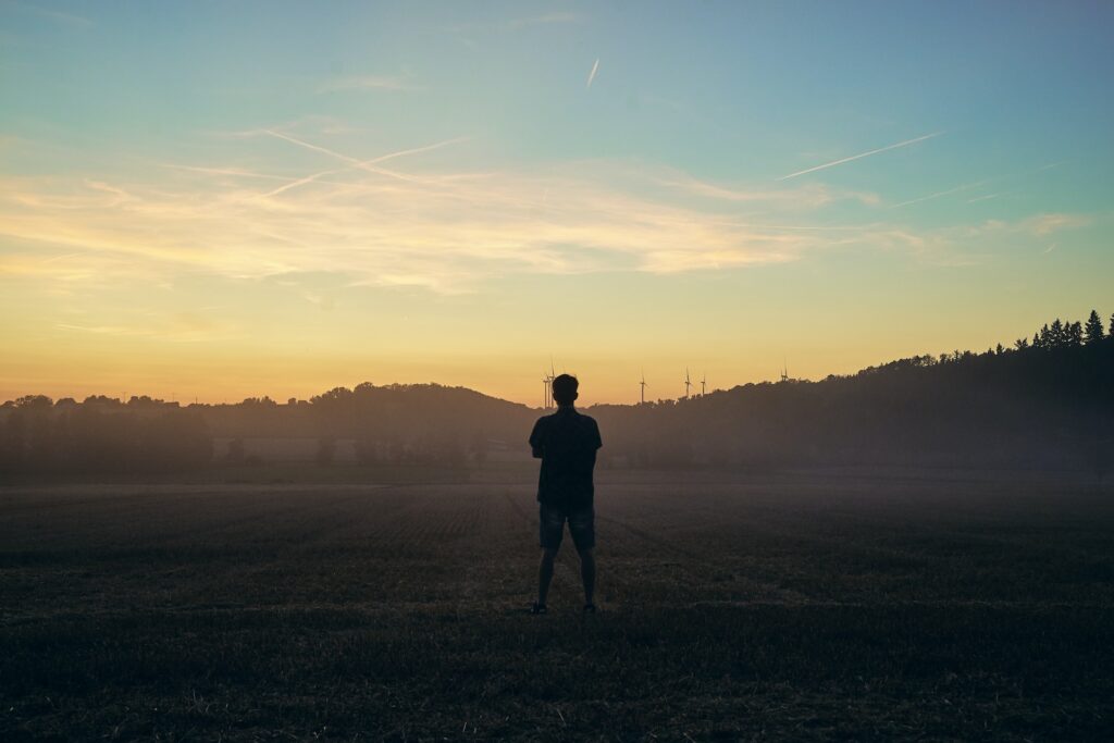 Homem parado, de costas e com os braços cruzados, em meio a um campo aberto.