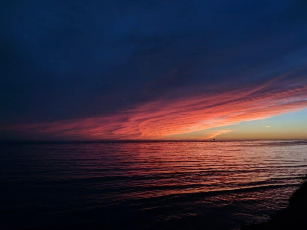 Mar calmo visto ao anoitecer, com reflexos do céu avermelhado na água.