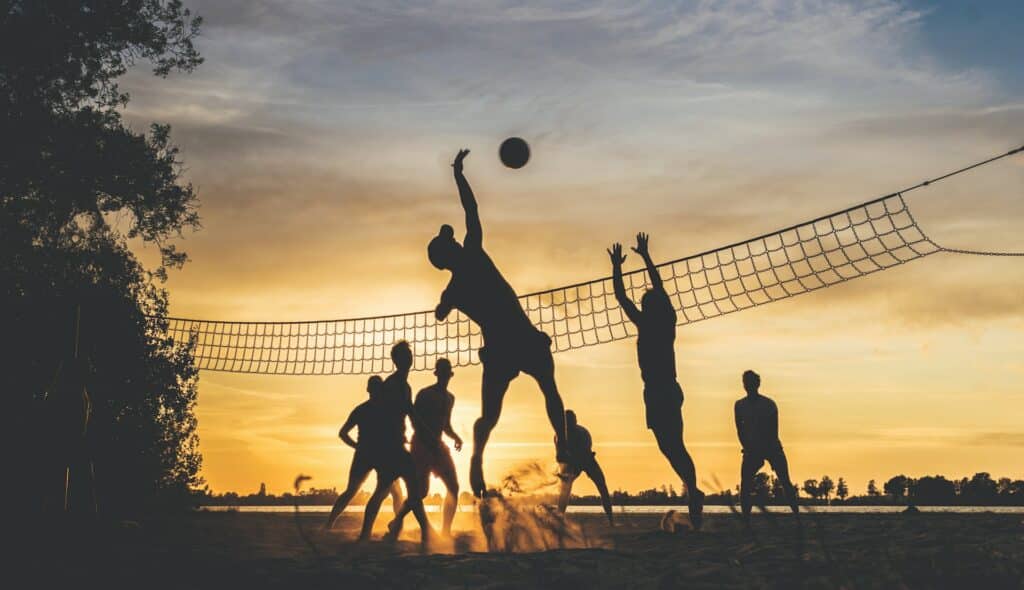 Silhueta de um grupo de homens praticando vôlei na praia durante o pôr-do-Sol.