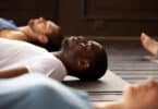 Homem deitado no chão de uma sala fazendo o yoga nidra com mais pessoas