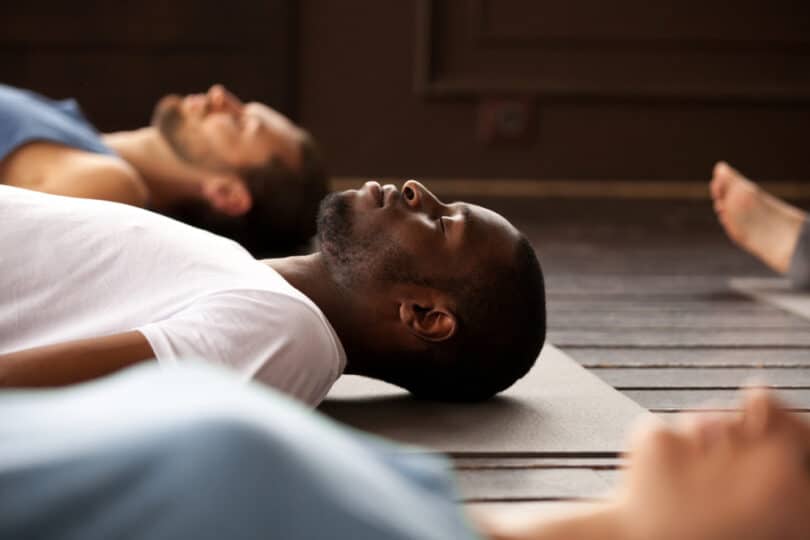 Homem deitado no chão de uma sala fazendo o yoga nidra com mais pessoas