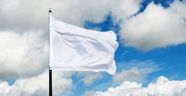 Bandeira branca hasteada no céu azul com algumas nuvens