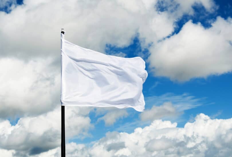 Bandeira branca hasteada no céu azul com algumas nuvens