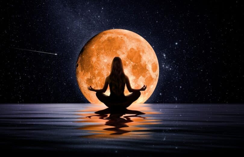 Silhueta de mulher sentada meditando sobre as águas com uma grande Lua dourada ao seu redor