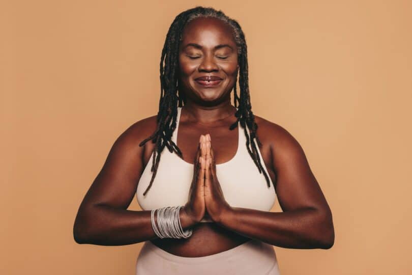 Mulher de olhos fechados e com as mãos na frente do peito meditando