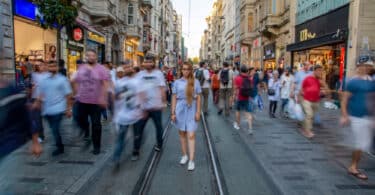 Várias pessoas desconhecidas caminhando na rua durante o dia. A maioria está desfocada.