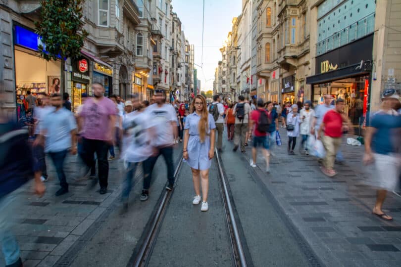 Várias pessoas desconhecidas caminhando na rua durante o dia. A maioria está desfocada.