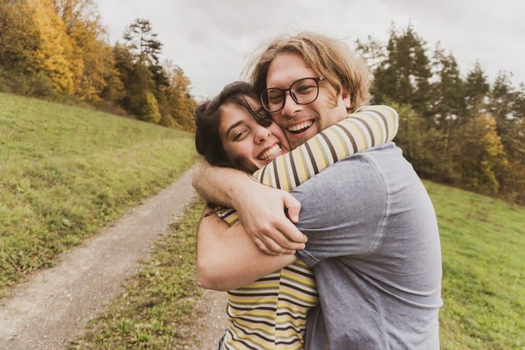 Mulher e homem se abraçando e sorrindo em meio a uma paisagem da natureza.