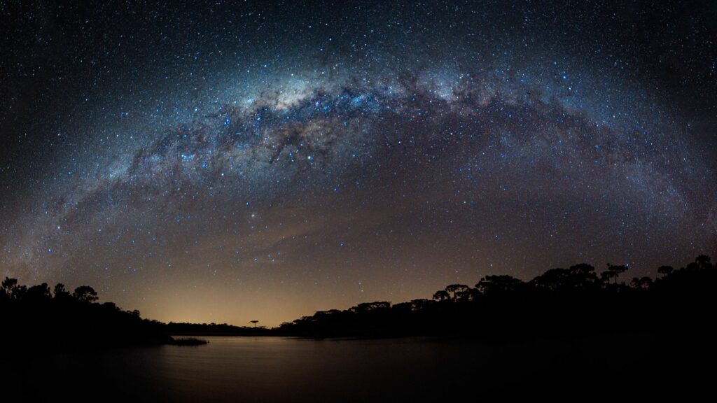 Imagem de um céu estrelado, árvores e um lago como parte da paisagem