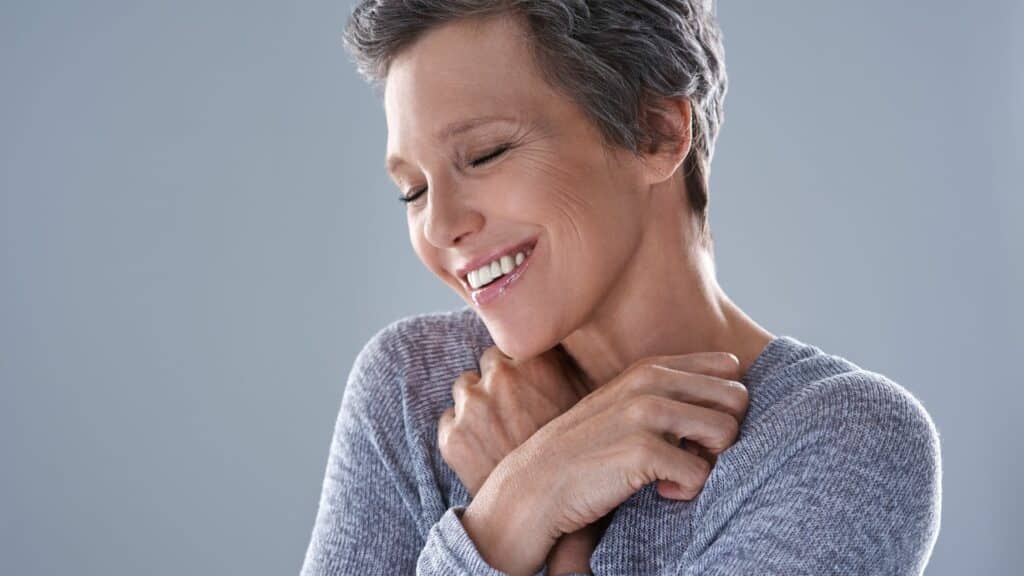 Imagem de uma mulher de meia idade abraçando a si mesma e sorrindo