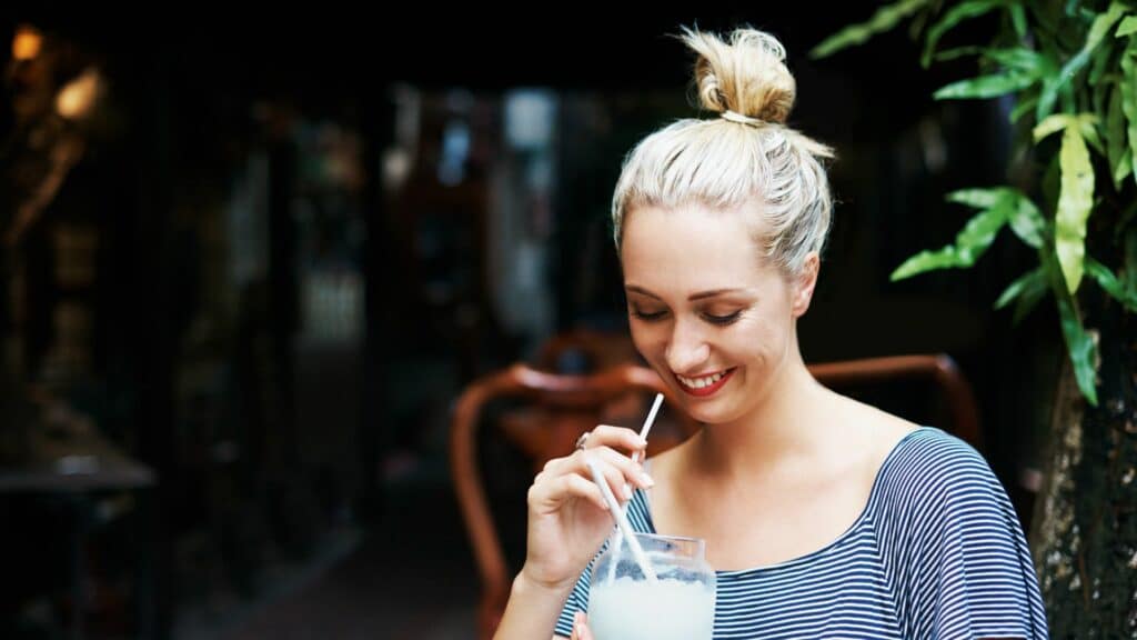 Imagem de uma mulher sorrindo e tomando um suco ao ar livre