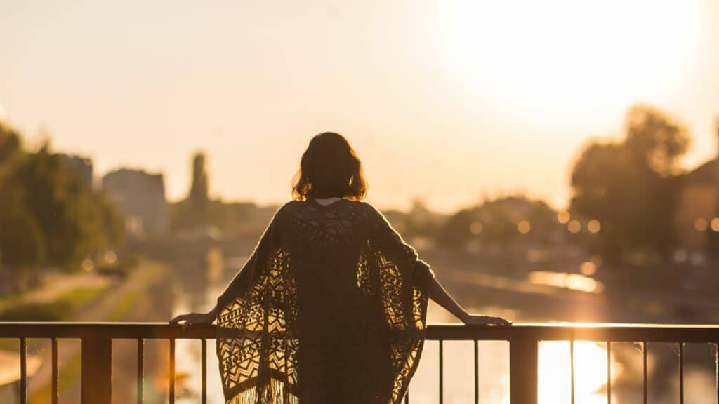 Imagem de uma mulher olhando ao horizonte em uma ponte, ao pôr do sol
