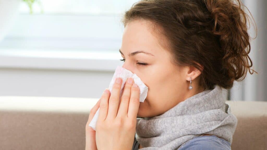 Imagem de uma mulher gripada limpando o nariz com papel
