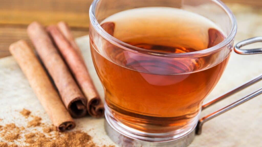 Imagem de uma xícara de chá de canela e canelas em pau e em pó do lado do chá