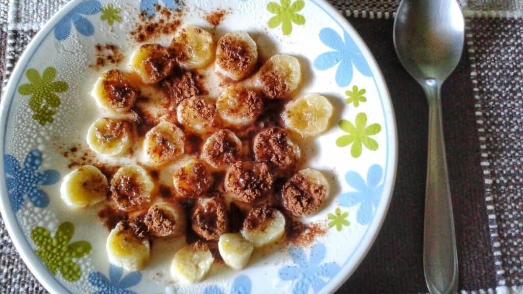 Imagem de um prato com rodelas de banana com canela e uma colher do lado
