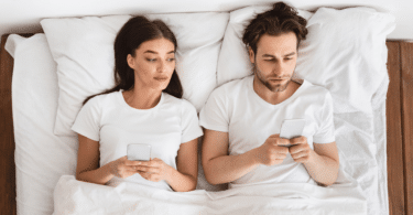 Casal deitado na cama mexendo no celular