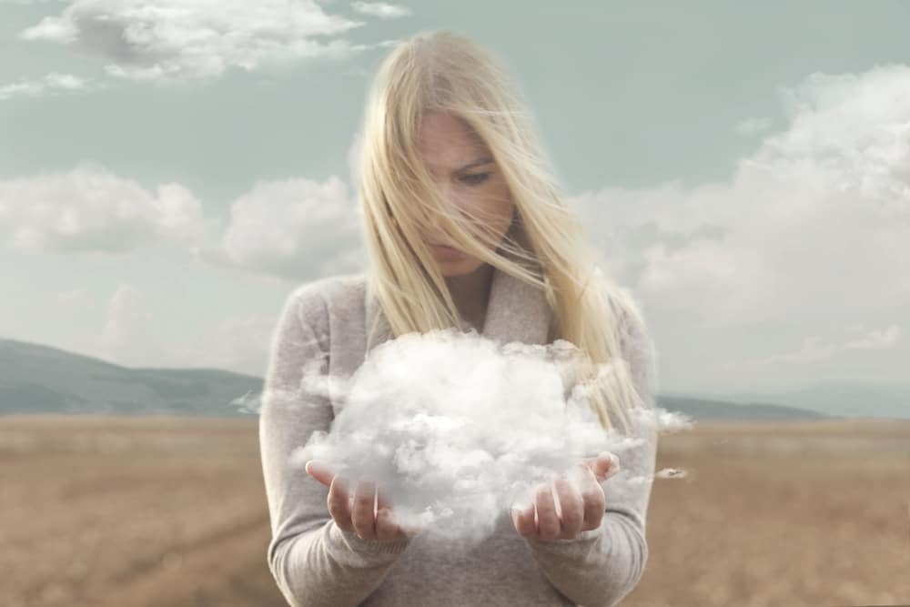 Mulher segurando uma nuvem em suas mãos e olhando para ela, com os cabelos ao vento.