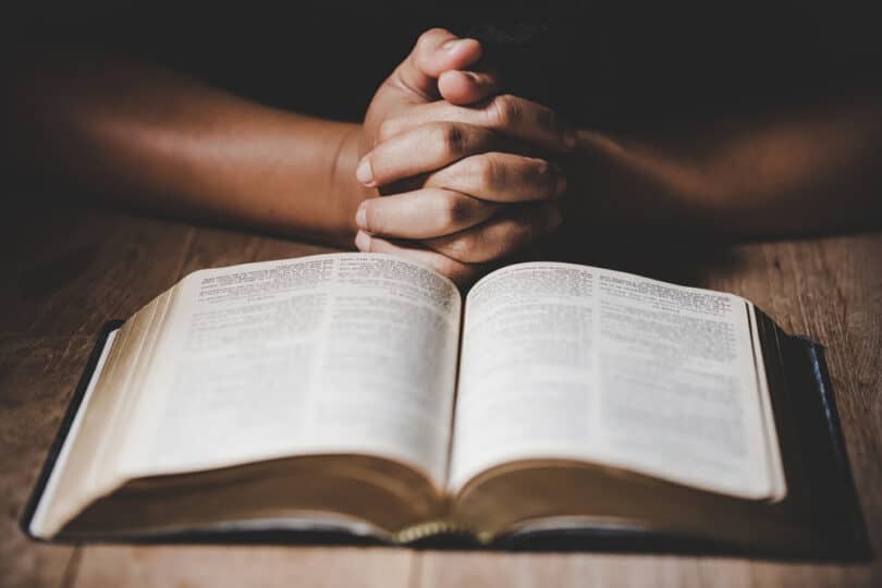 Mãos cruzadas sobre uma mesa com uma Bíblia aberta