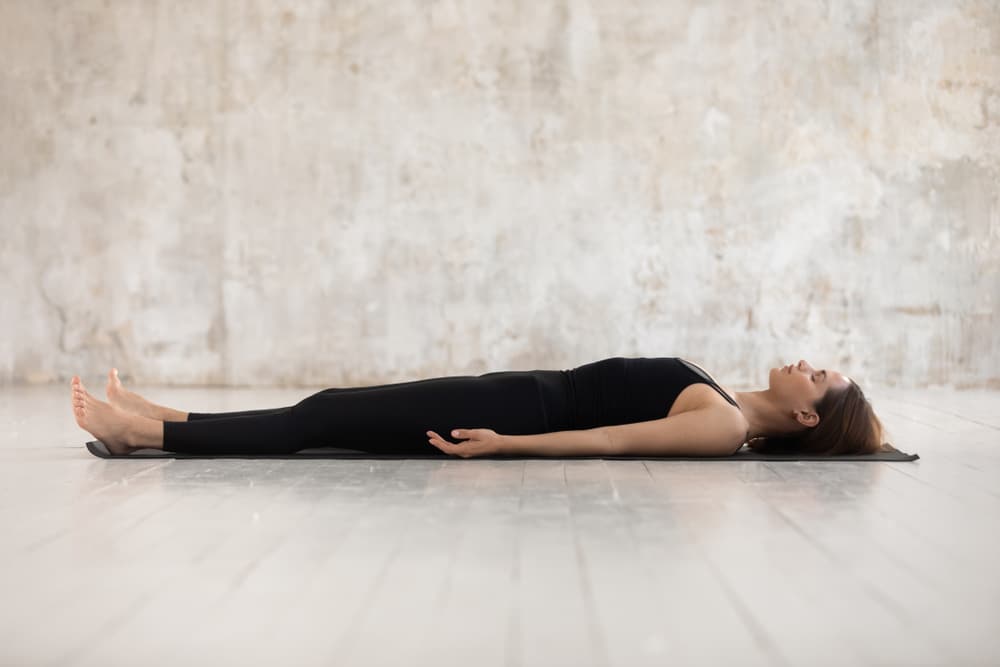 Mulher realizando a postura savasana da Yoga em ambiente fechado