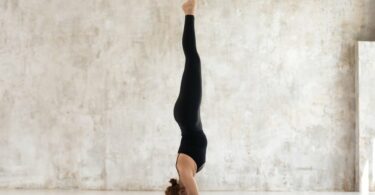 Mulher fazendo a posição sirsasana sobre um tapete de Yoga em um ambiente interno de cores claras