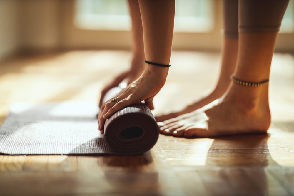 Mulher enrolando um tapete de Yoga dentro de uma sala ensolarada