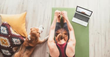 Vista superior de uma mulher fazendo Yoga em casa ao lado de seu cachorro e com o auxílio de um computador