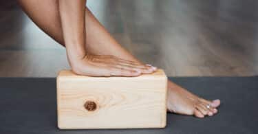 Mão apoiada sobre um bloco de Yoga cor de madeira