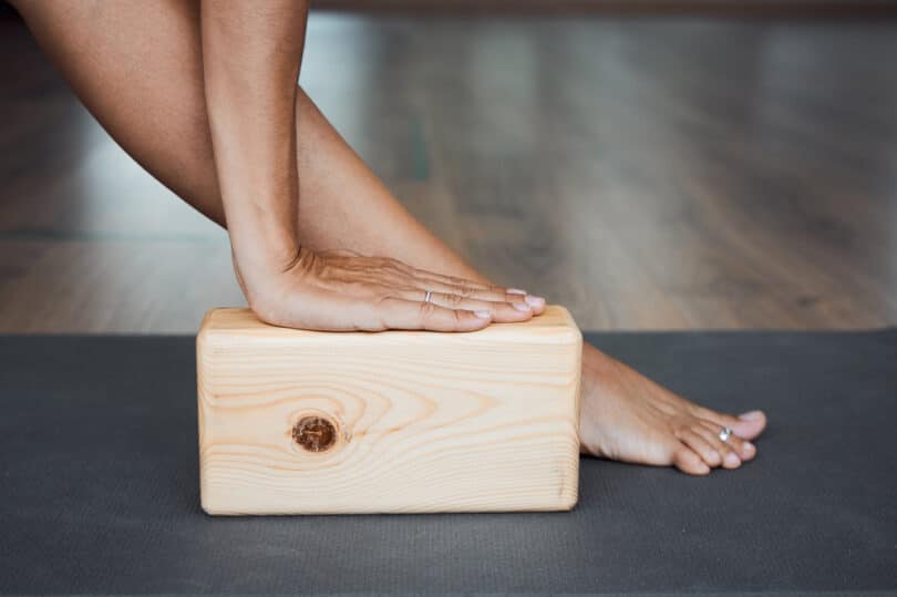 Mão apoiada sobre um bloco de Yoga cor de madeira
