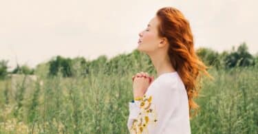 Mulher rezando de olhos fechados no meio da natureza