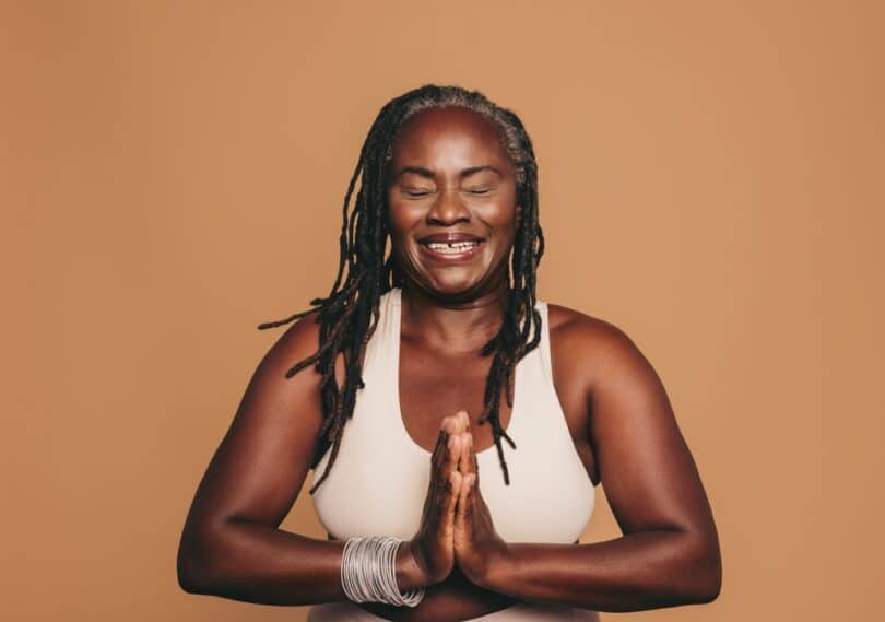 Mulher meditando com as mãos juntas na frente do peito e grande sorriso no rosto